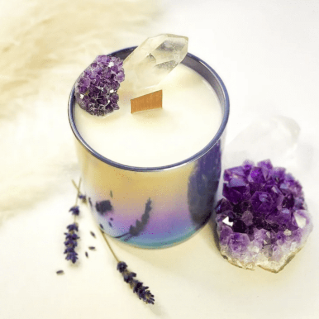 Bougie blanche entourée de cristaux violets et transparents et de fleurs de lavande.