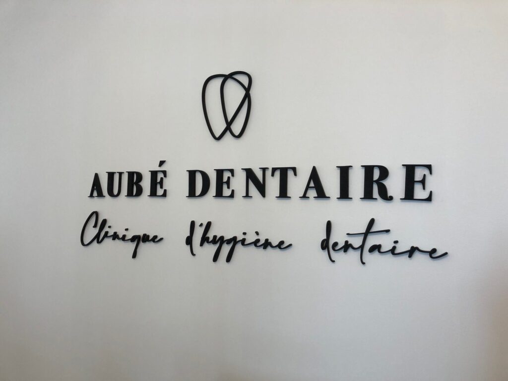 Logo d'Aubé Dentaire en gros sur un mur blanc à l'intérieur du bâtiment.